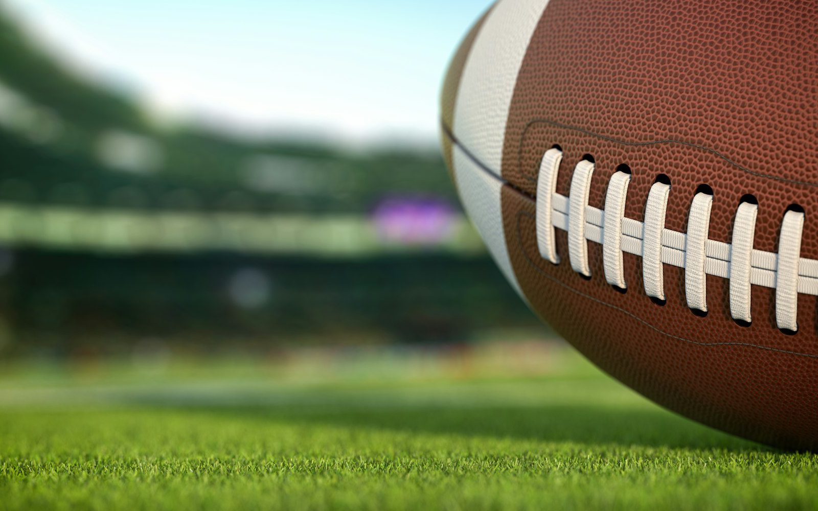 American football ball on grass of football arena